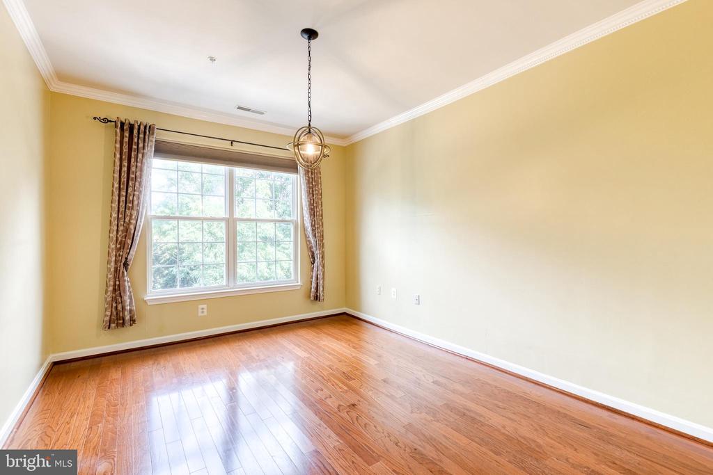 Empty dining room with hardwood floors, a large curtained window, and a hanging light.