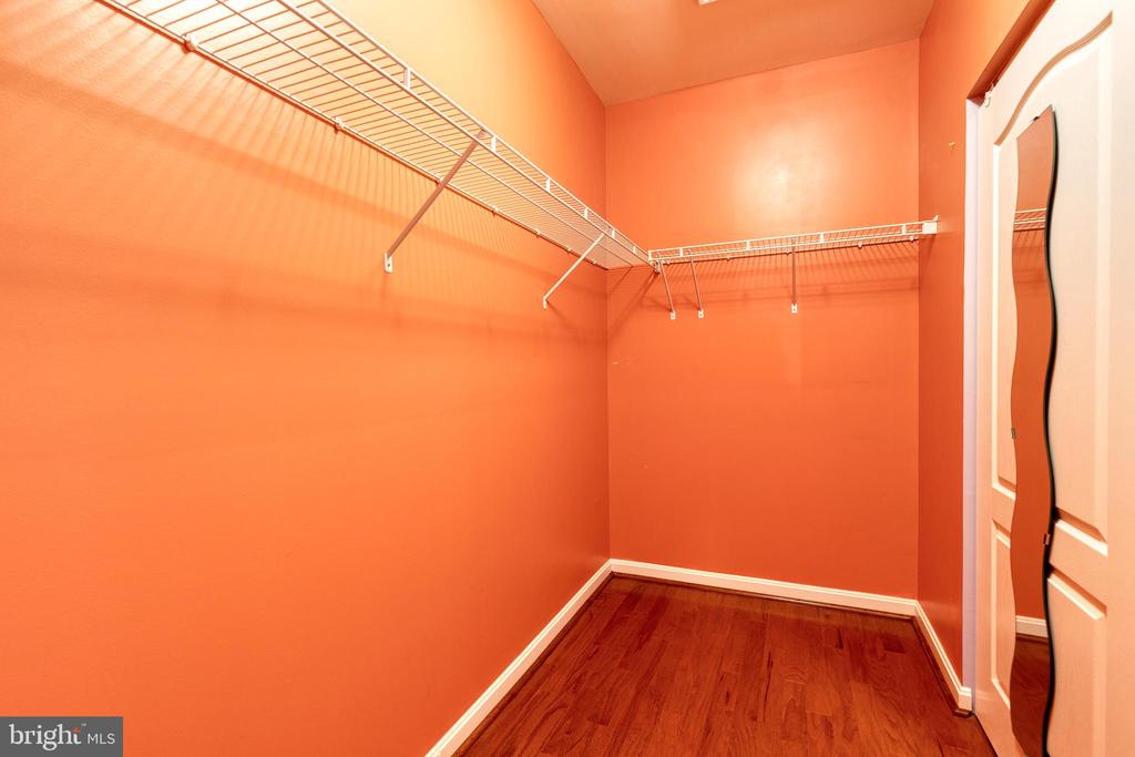 Walk-in closet with white wire shelving, orange walls, and hardwood flooring.