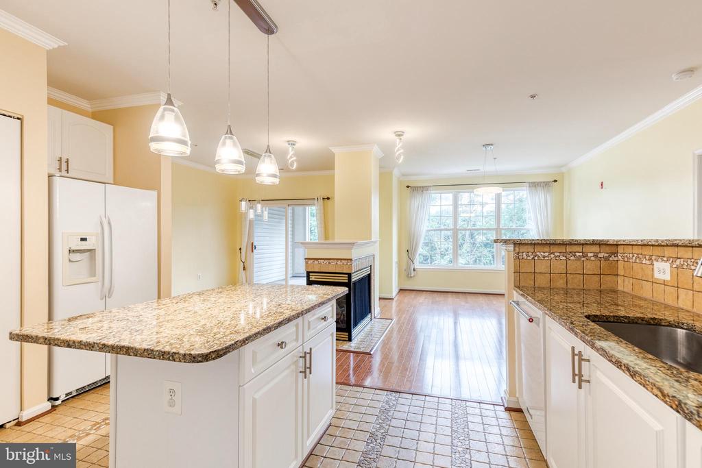 Kitchen with granite island and counters, opening to a living area with a fireplace and large windows.
