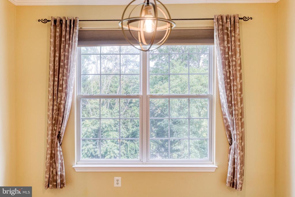 Large gridded window framed by patterned curtains, with leafy trees outside and a pendant light above.