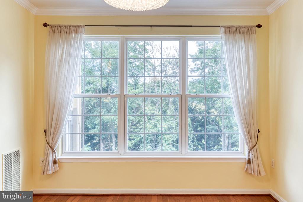 Room with a large three-section window framed by sheer curtains, yellow walls, and hardwood flooring.