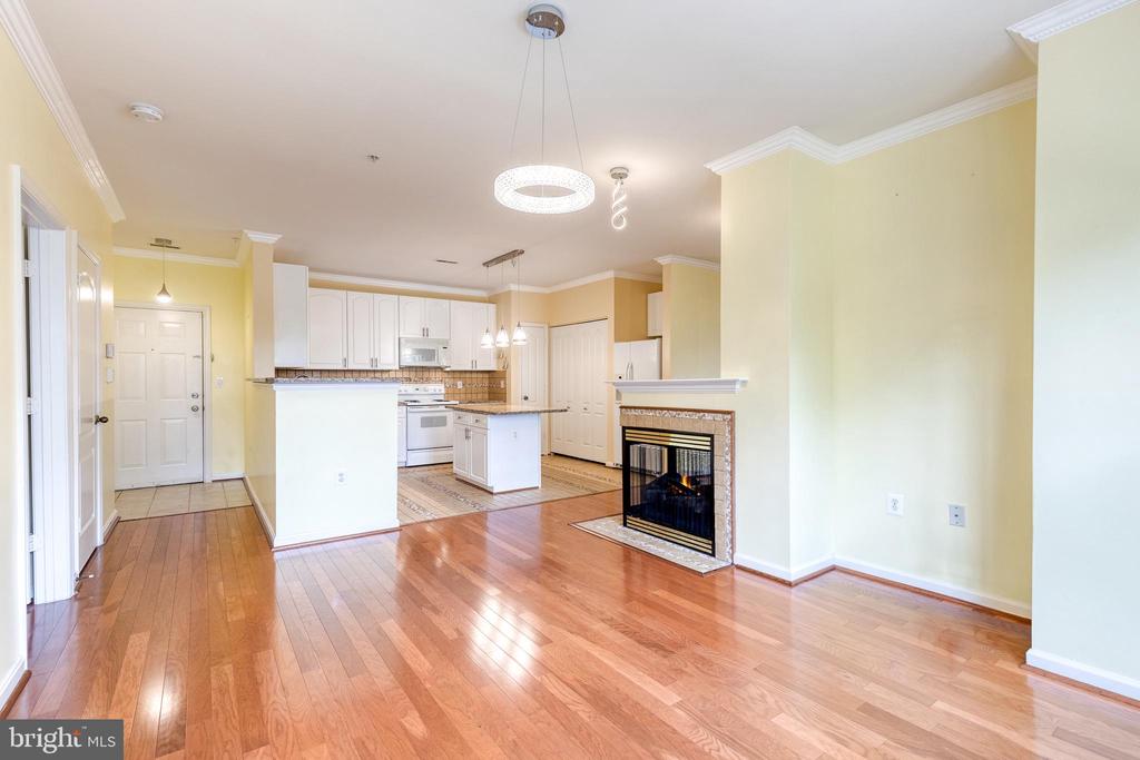 Open living and kitchen area with hardwood floors, white cabinets and island, and a fireplace.