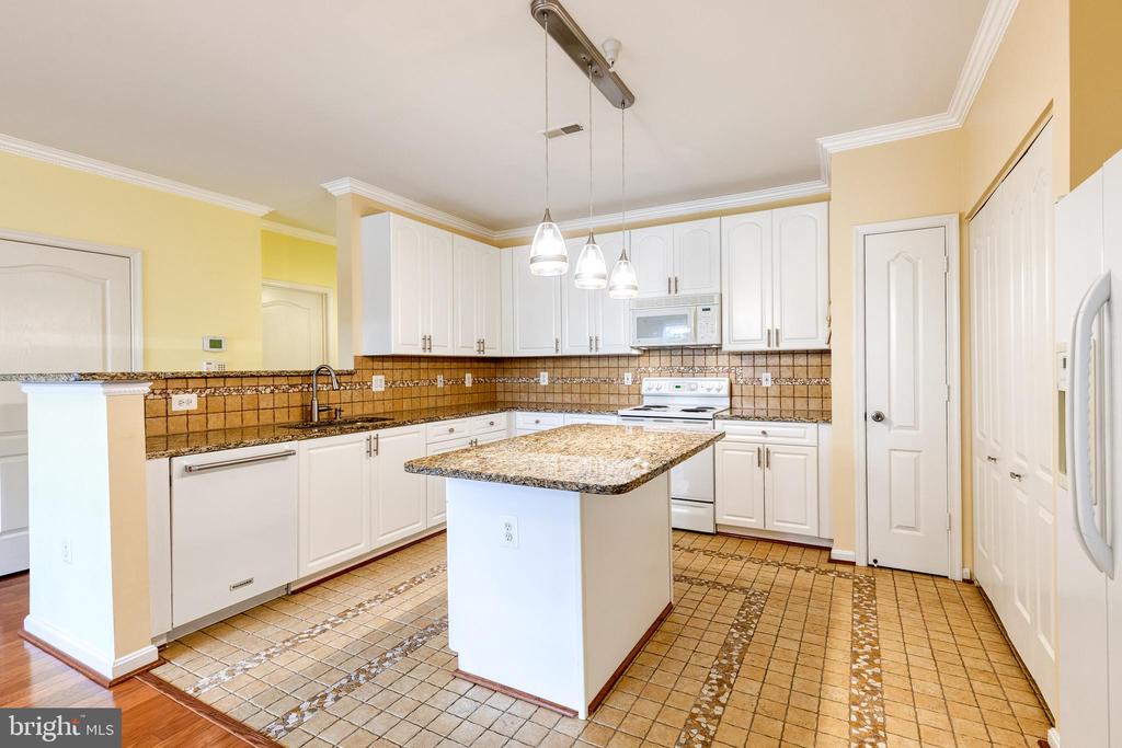 Kitchen with white cabinetry, granite-topped island, tiled backsplash, and three pendant lights.