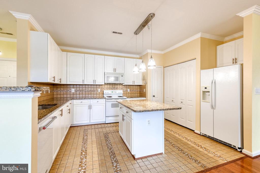 Kitchen with white cabinetry, a granite-topped island, tan tile floors, and pendant lighting.