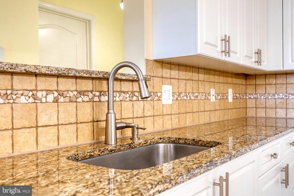 Kitchen sink with an arched faucet, granite countertops, white cabinets, and a tan tile backsplash.