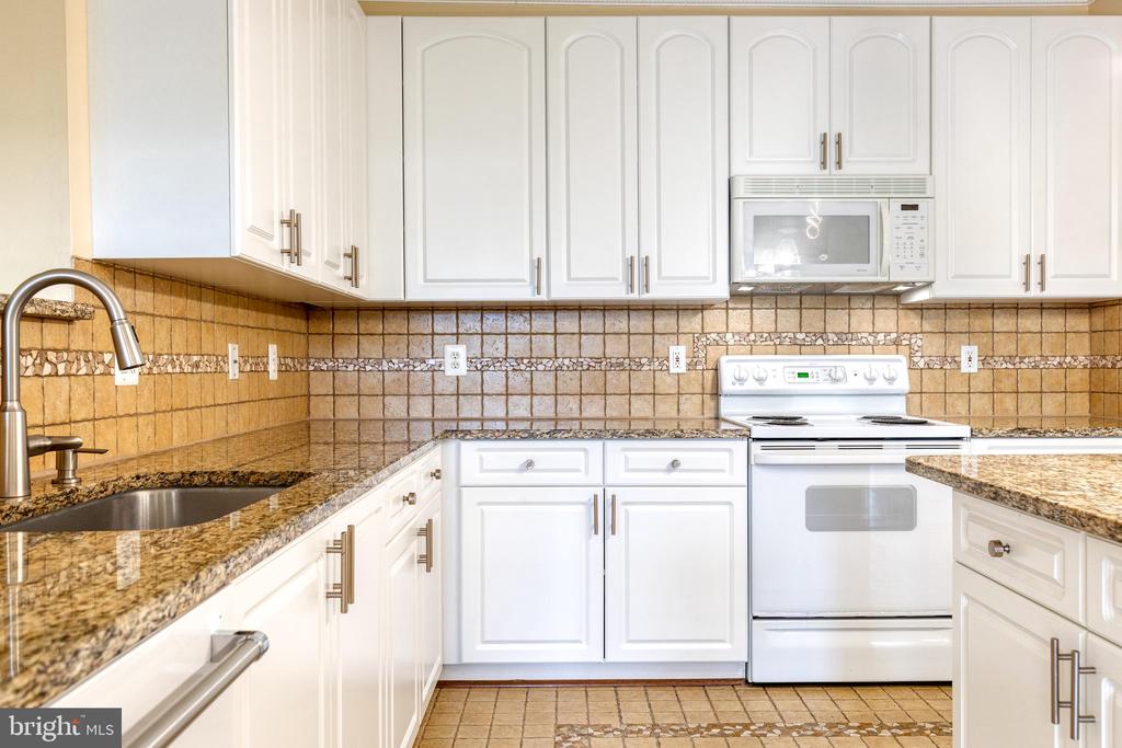 Kitchen with white cabinets, granite counters, tan tile, and a white electric range.