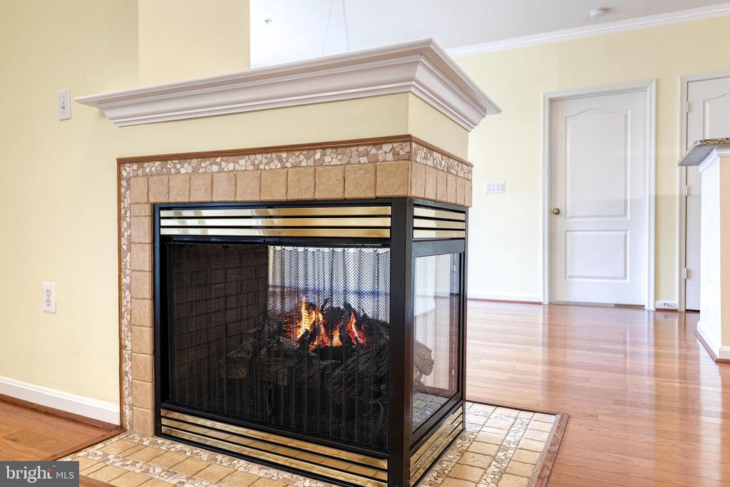 Three-sided stone fireplace with a lit fire in a vacant room with hardwood floors.