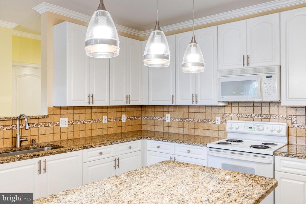 Kitchen with white cabinets, tan tile backsplash, granite counters and a large island.