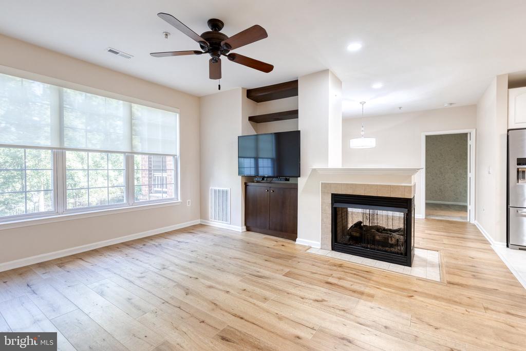 Living room with wide windows, light wood floors, built-in TV shelving, and a tiled fireplace.