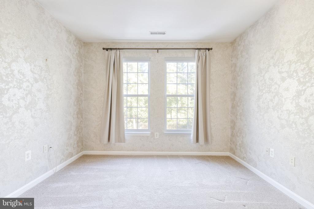 Vacant carpeted bedroom with patterned wallpaper and two curtained windows.