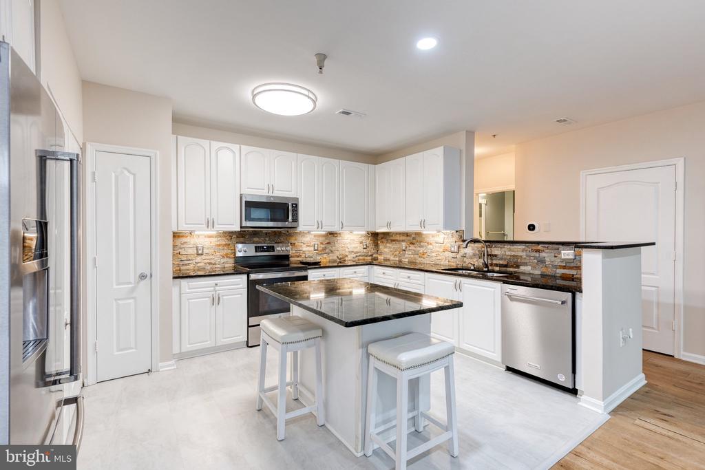 Kitchen with white cabinetry, stainless steel appliances, stone backsplash, and a central island with two stools.