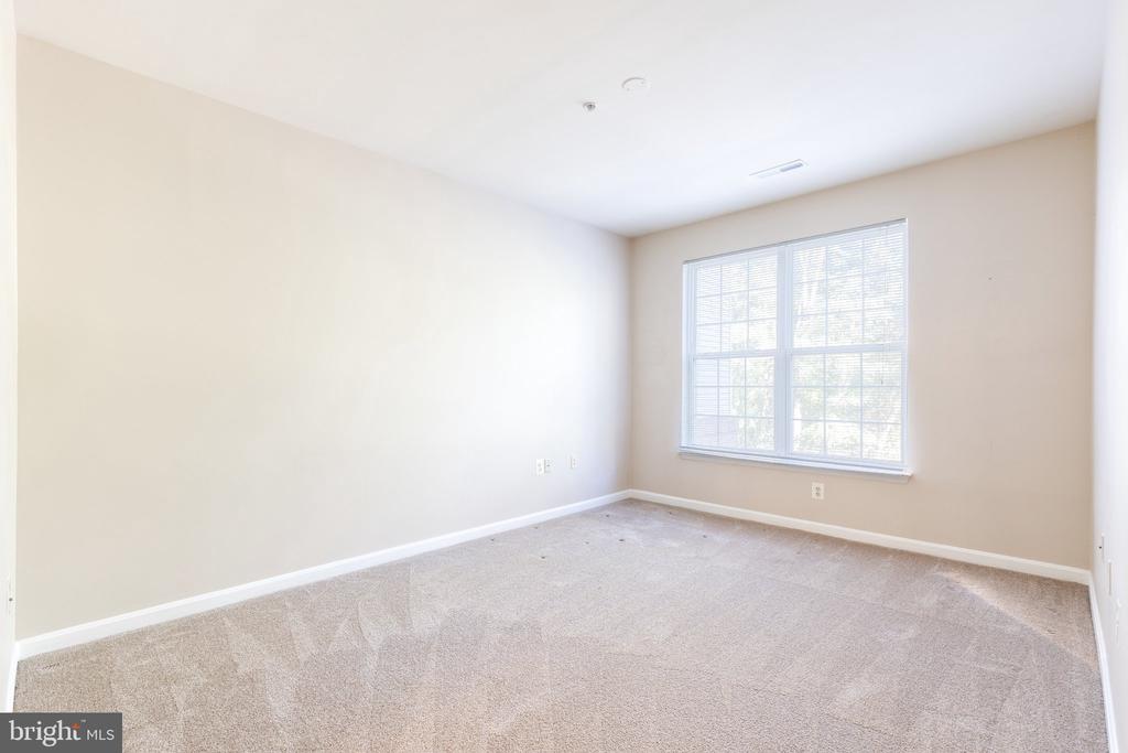 Empty carpeted room with a large window and white blinds.