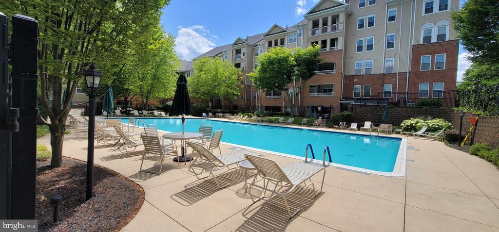 Outdoor swimming pool and furnished deck beside a multi-story apartment building.