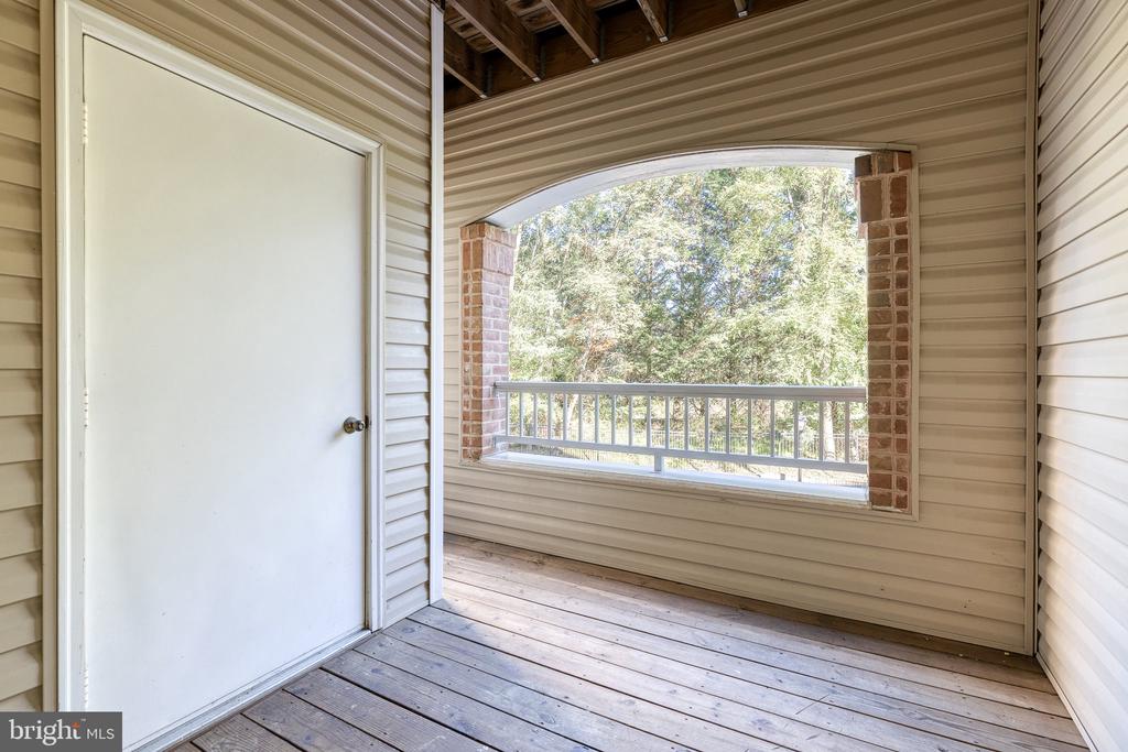 Covered porch with wood-plank flooring and a wide opening overlooking trees.