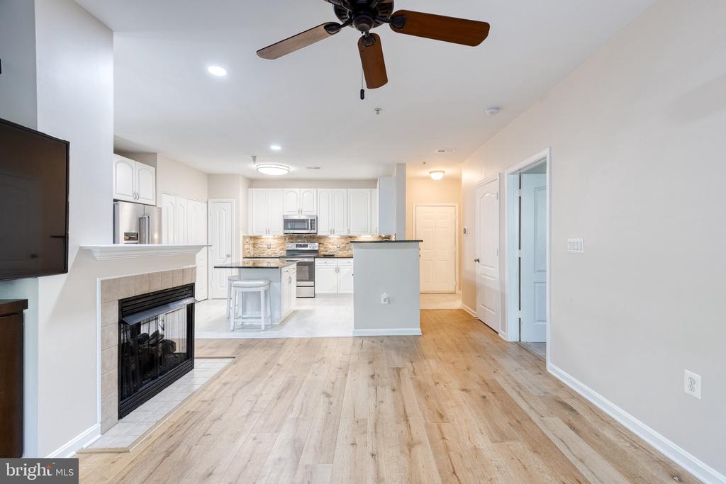 Open living room and kitchen with wood-look floors, tiled fireplace, white cabinets, and ceiling fan.