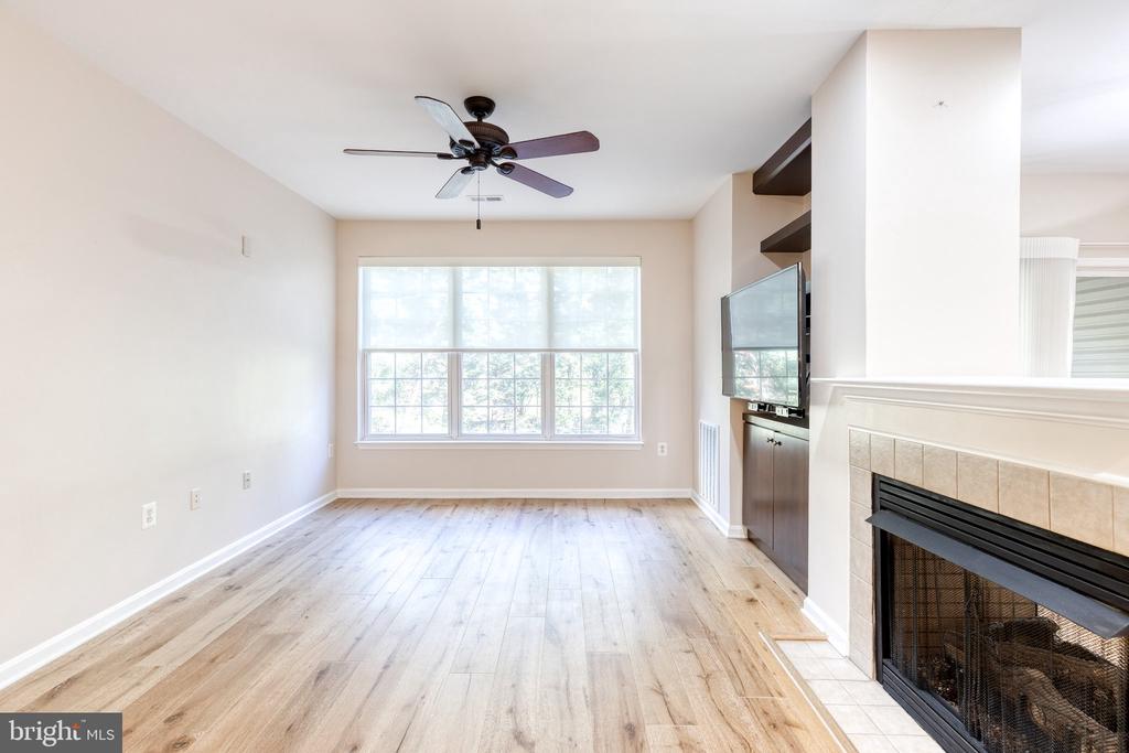 Empty living room with light wood floors, a large window, and a tiled fireplace.