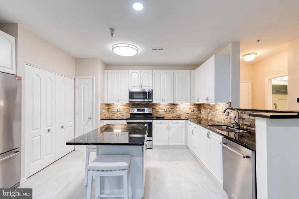 Renovated kitchen with white cabinets, black granite counters, a central island, and stone backsplash.