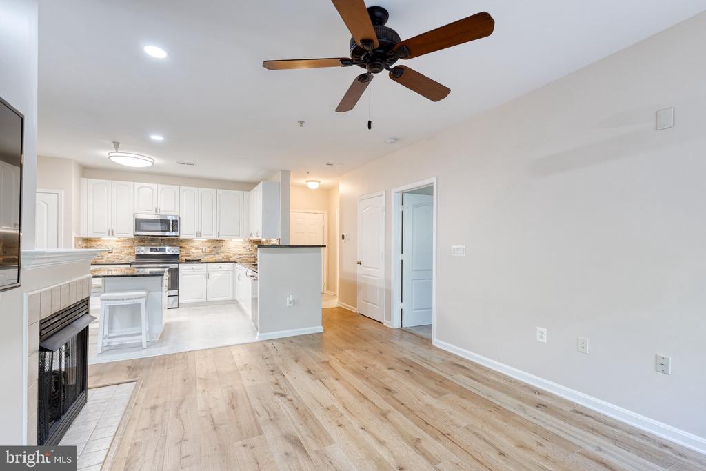 Open condo living area and kitchen with light wood floors, white cabinets, and a fireplace.