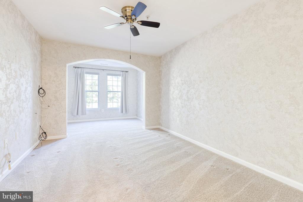 Empty carpeted room with a ceiling fan and arched opening to a curtained window alcove.