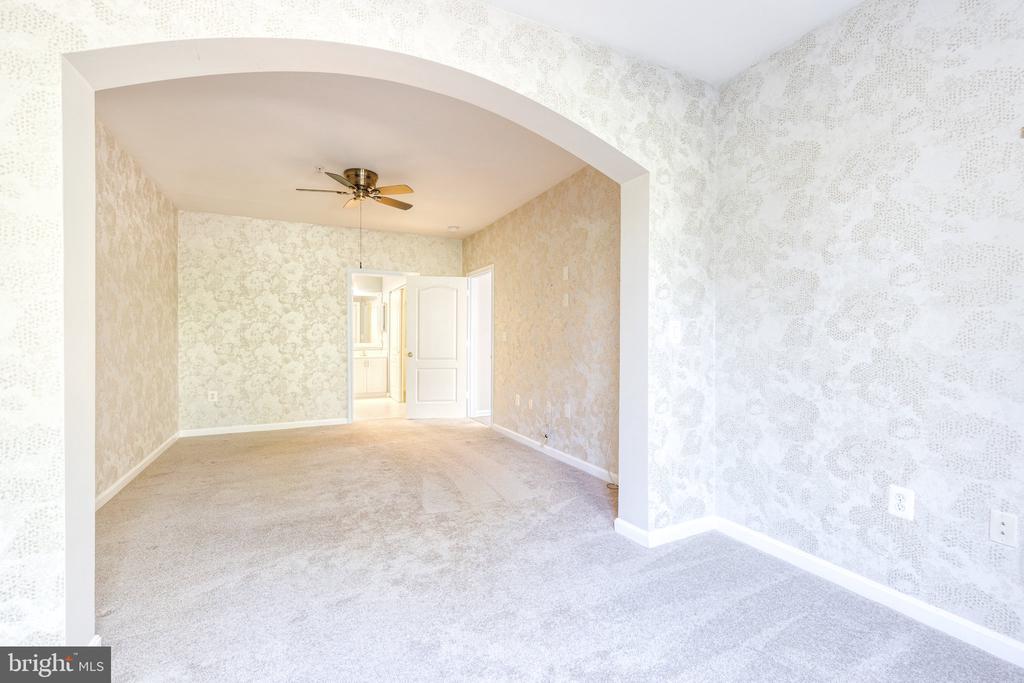 Empty carpeted living room with patterned wallpaper, a wide archway, and a ceiling fan.