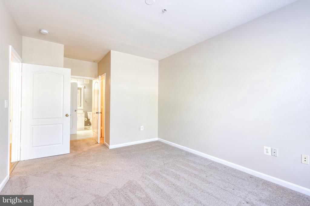 Empty carpeted bedroom with neutral walls and an open doorway to the bathroom.