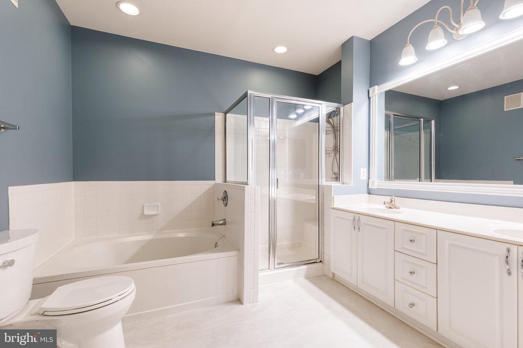 Bathroom with a white tub, glass-enclosed shower, and long vanity against blue walls.