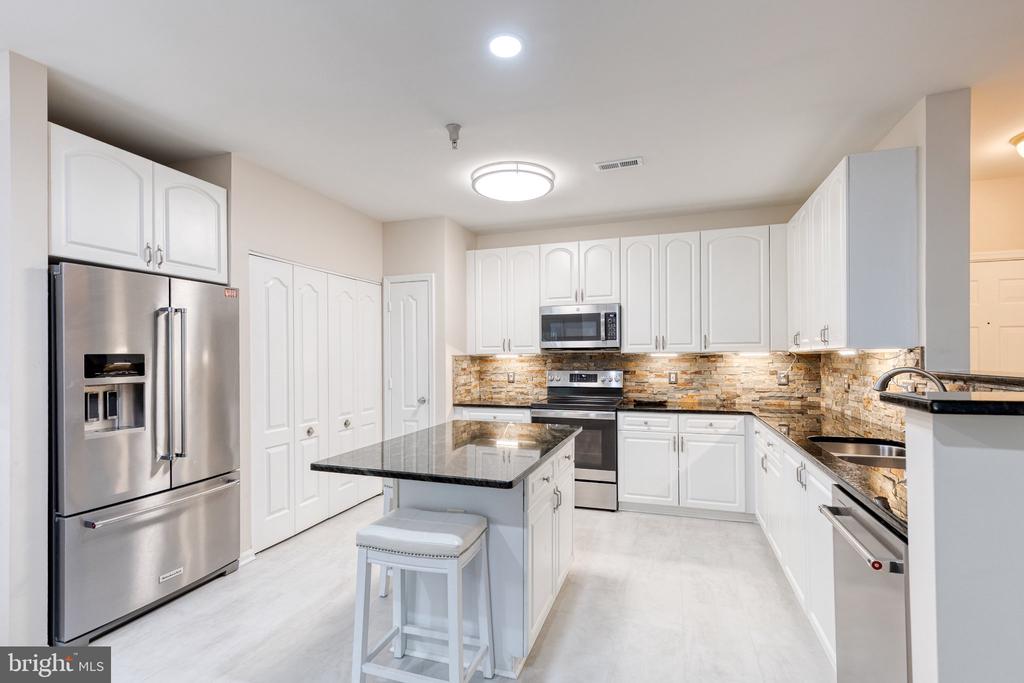 Modern kitchen with white cabinets, stainless steel appliances, and a black island beside a multicolored tile backsplash.