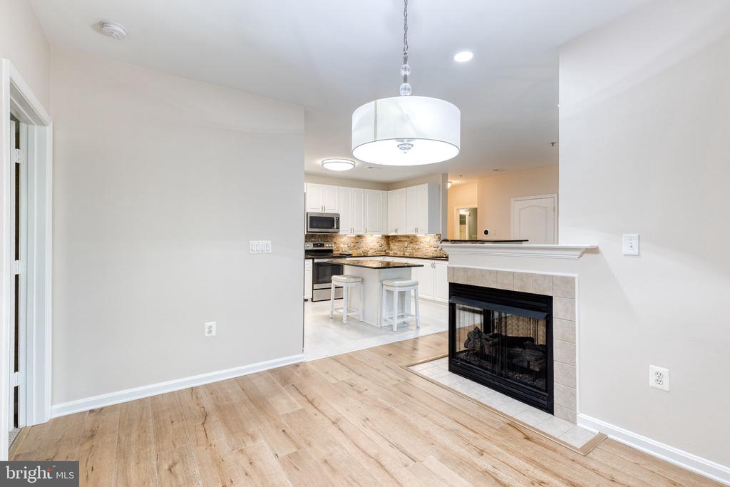 Open kitchen with white cabinets, breakfast bar, light wood flooring, and a tiled fireplace.