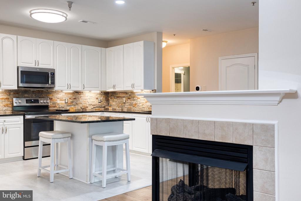 Kitchen with white cabinets, a stone backsplash, an island, and a fireplace.