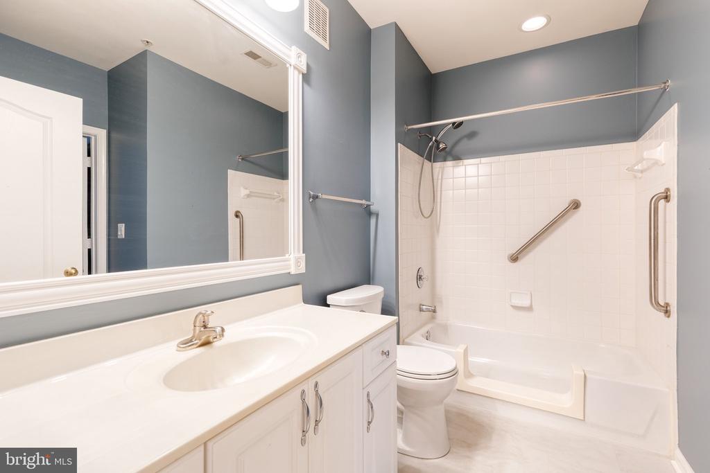 Bathroom with a white vanity and large mirror, bathtub, tiled shower, and grab bars.