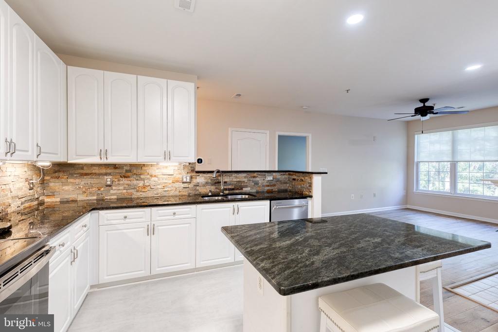 Kitchen with white cabinetry, a stone backsplash, and a large granite island.