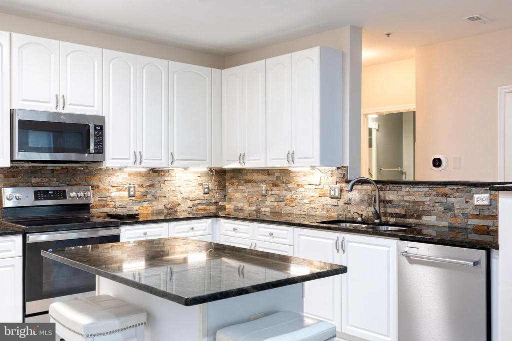 Kitchen with white cabinets, stainless steel appliances, stone backsplash, and a black stone island.