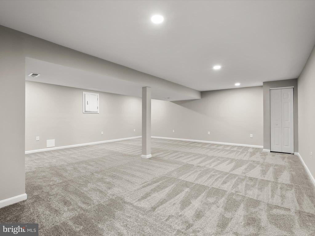 Finished basement with patterned carpet, recessed lights, and a central support column.