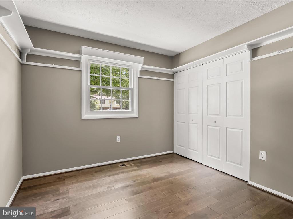 Empty bedroom with hardwood floors, a window, and large white paneled closet doors.