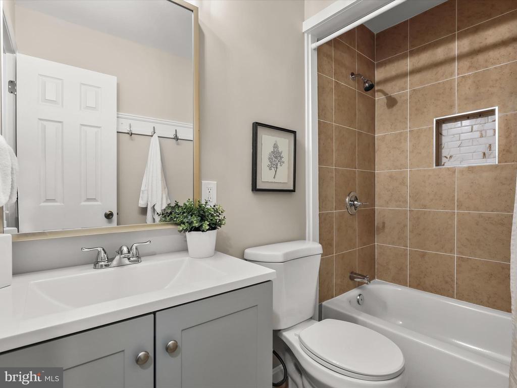 Bathroom with gray vanity, toilet, and bathtub featuring a brown tiled shower surround.