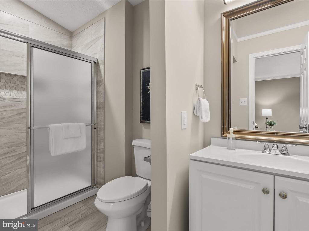 Bathroom with a marble-look tiled shower, white vanity, and large framed mirror.