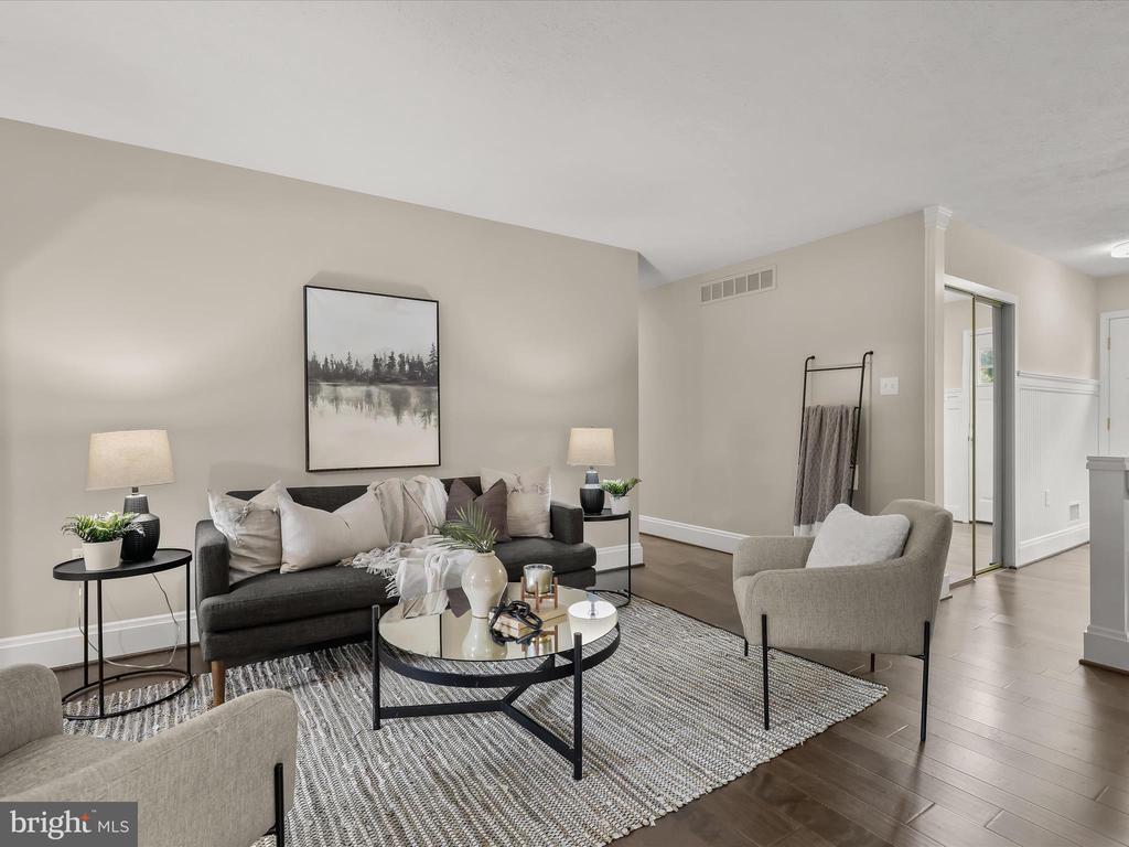 Staged living room with a dark sofa, glass coffee table, patterned rug, and neutral armchairs.