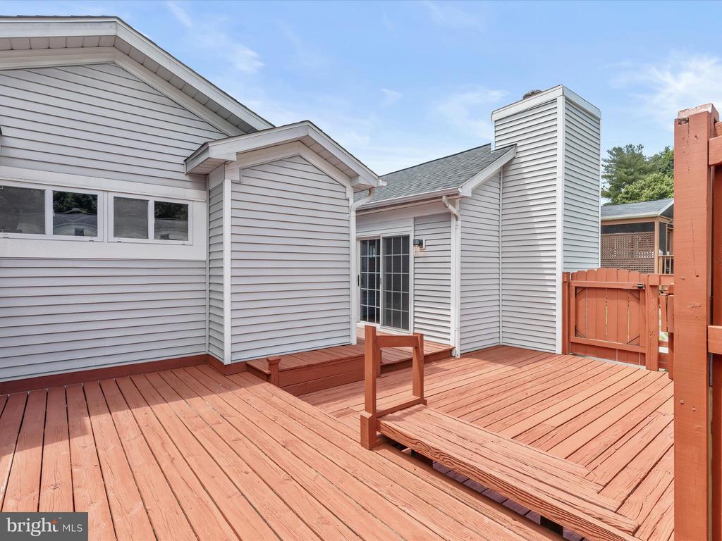 Rear deck with reddish wood planks, steps, and a gate beside gray siding and sliding glass doors.