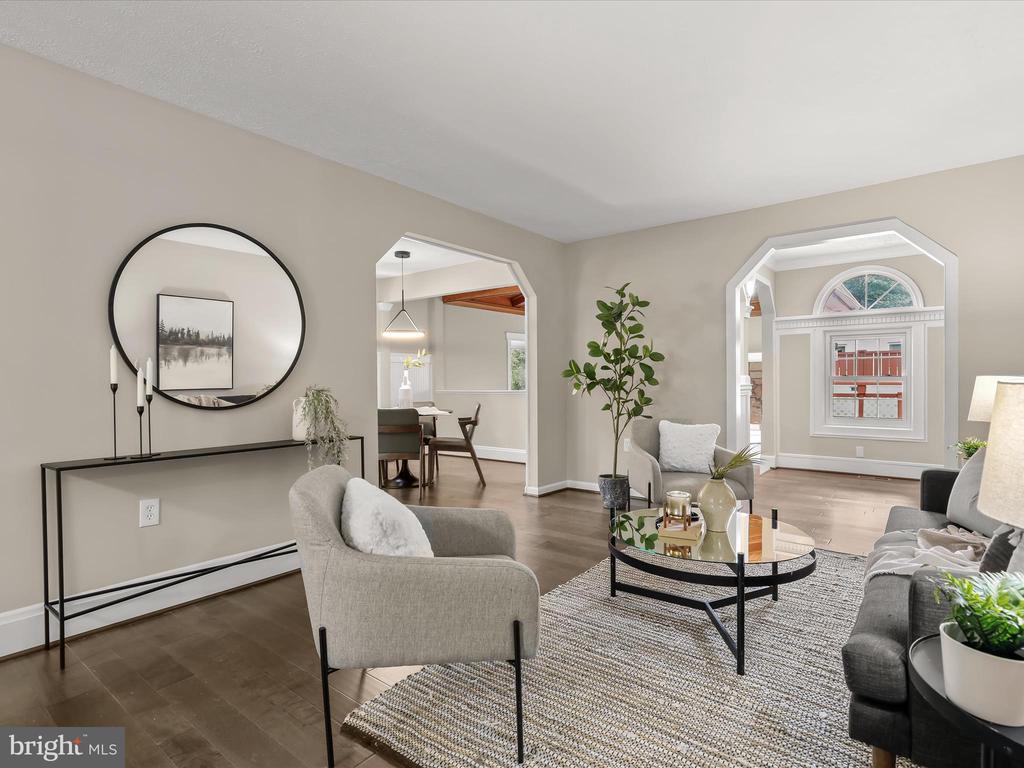 Staged living room with gray seating, dark wood floors, and arched openings to adjoining rooms.