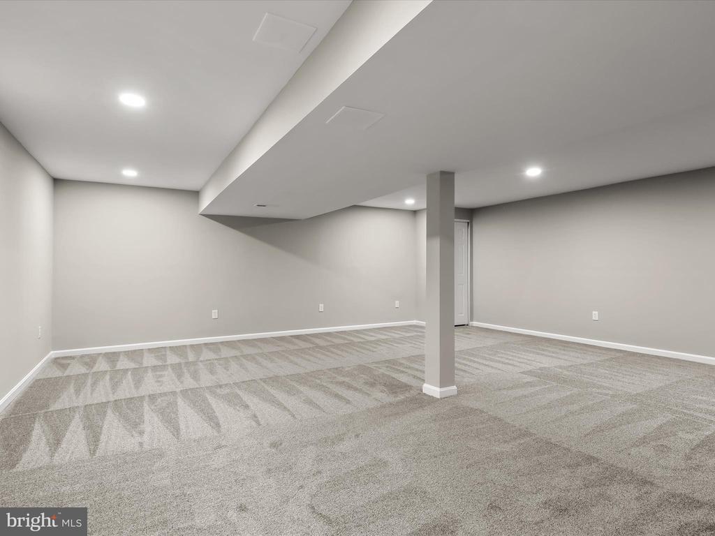 Vacant finished basement with patterned carpet, recessed lighting, and a central support post.