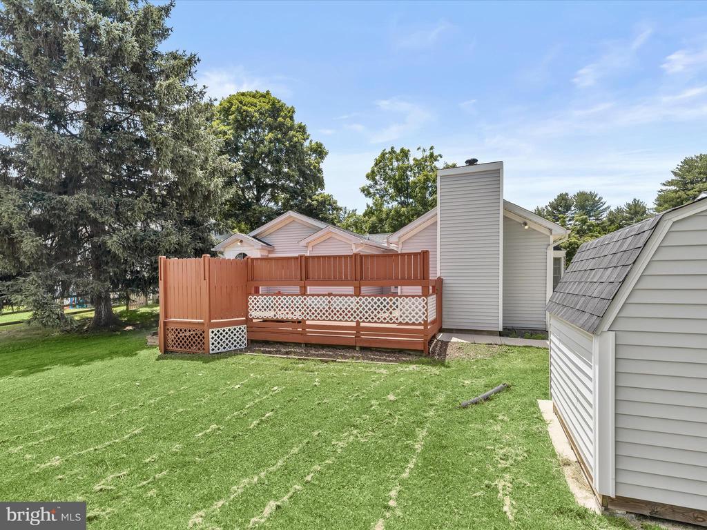 Home’s backyard with a fenced raised deck, broad lawn, mature trees, and a small shed.