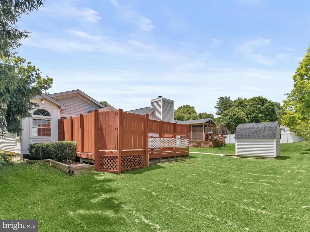 Backyard with a raised wooden deck, broad green lawn, and small white storage shed.