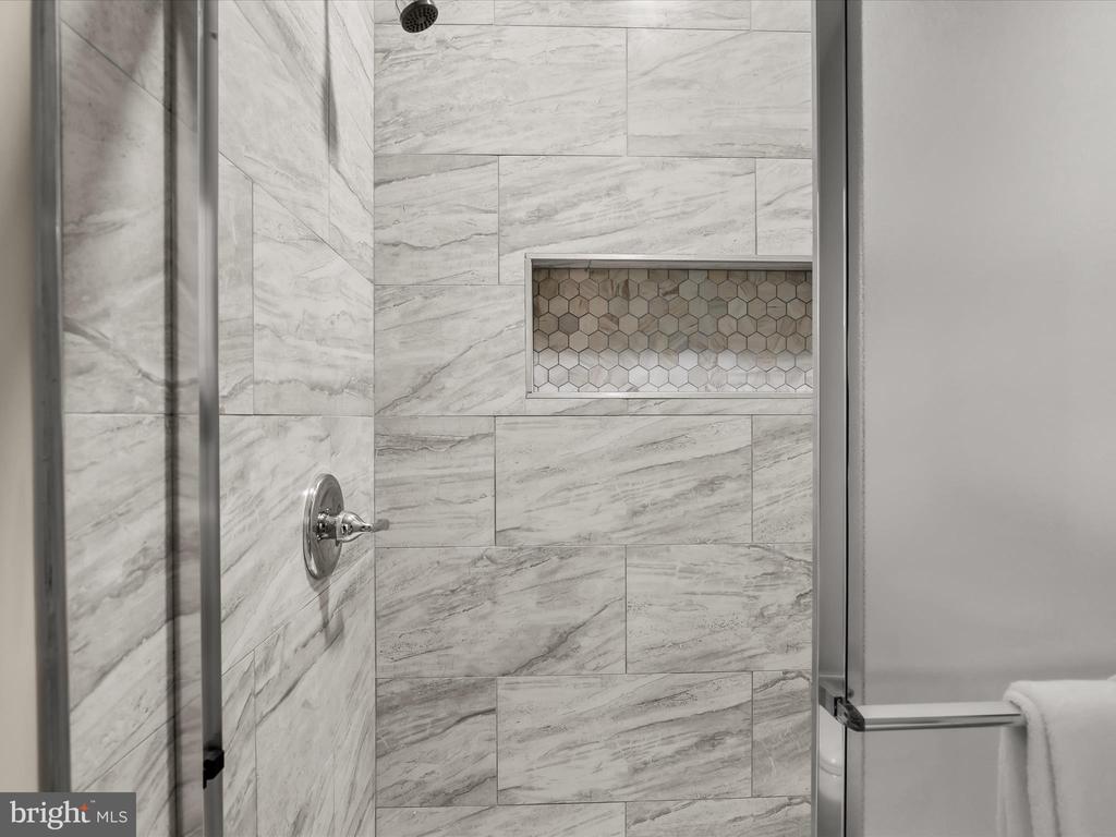 Walk-in shower with gray-veined tile, a hexagonal-tile niche, and glass enclosure.