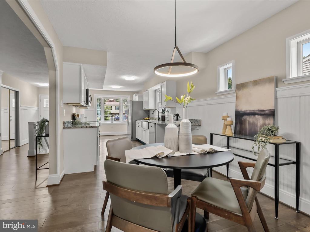 Dining room with a black oval table and upholstered chairs, open to a bright white kitchen.