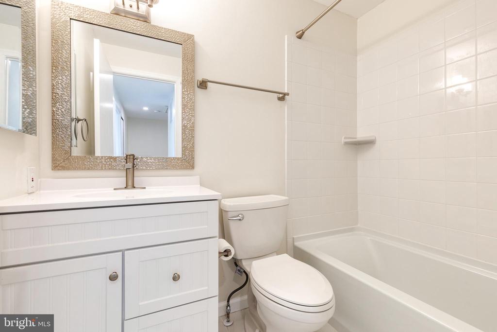 Bathroom with a white vanity, framed mirror, toilet, and tiled bathtub.