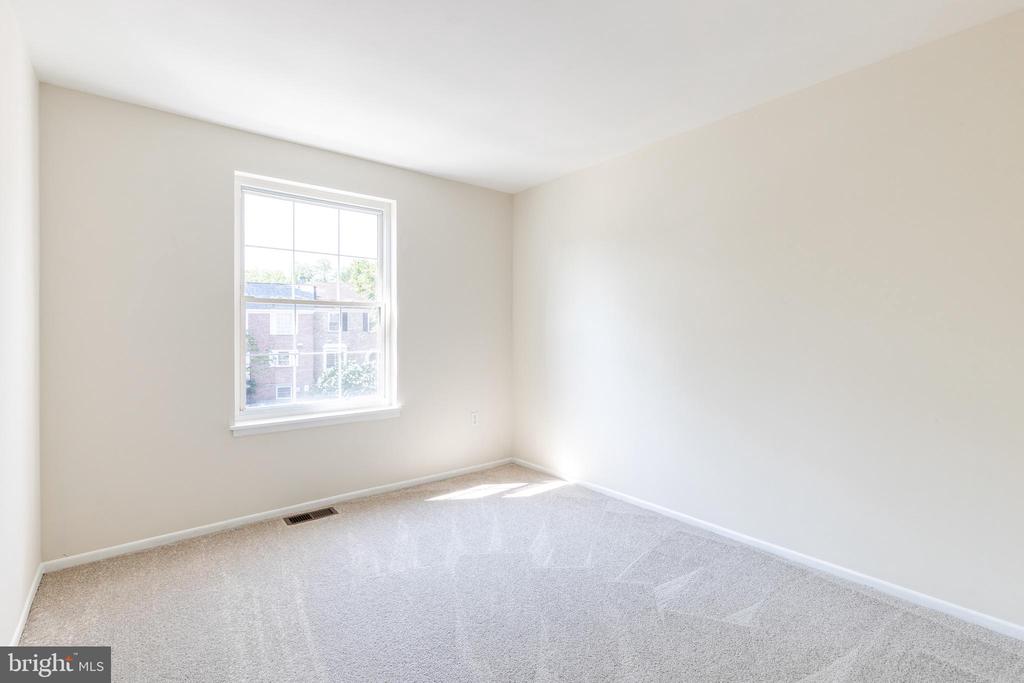 Empty carpeted room with neutral walls and a large window overlooking a brick building.