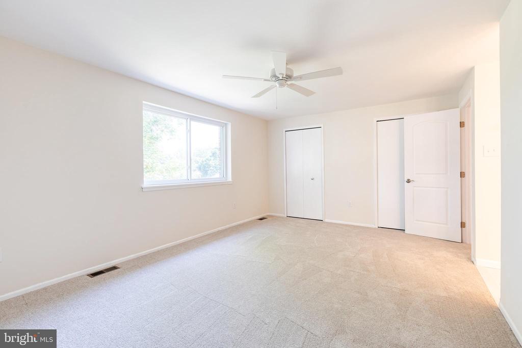 Empty carpeted bedroom with a large window, two closets, and a ceiling fan.