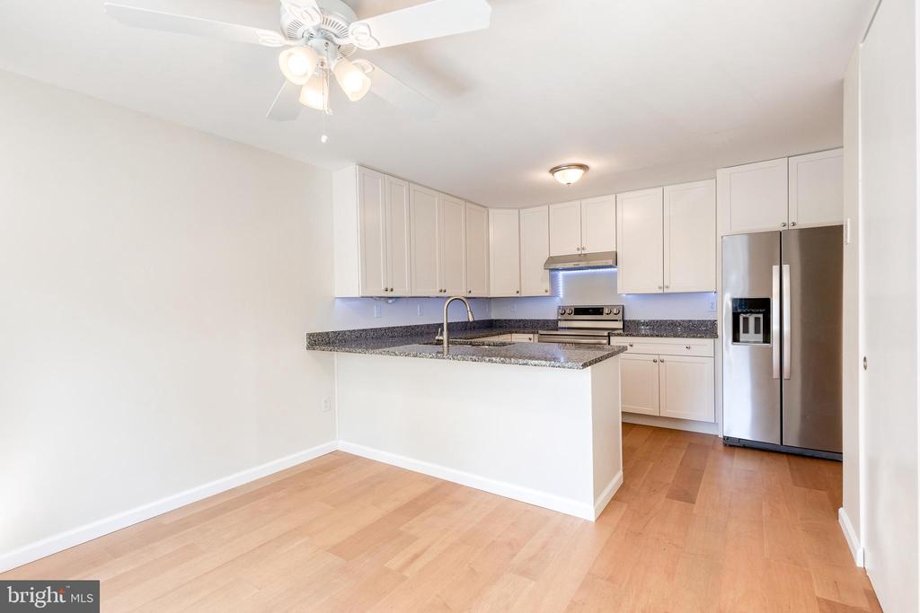 Kitchen with white cabinets, granite peninsula, stainless steel appliances, and light wood floors.