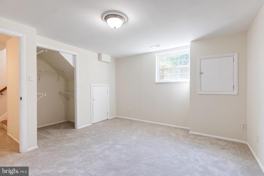 Vacant carpeted room with an open wire-shelved closet and a small high window.