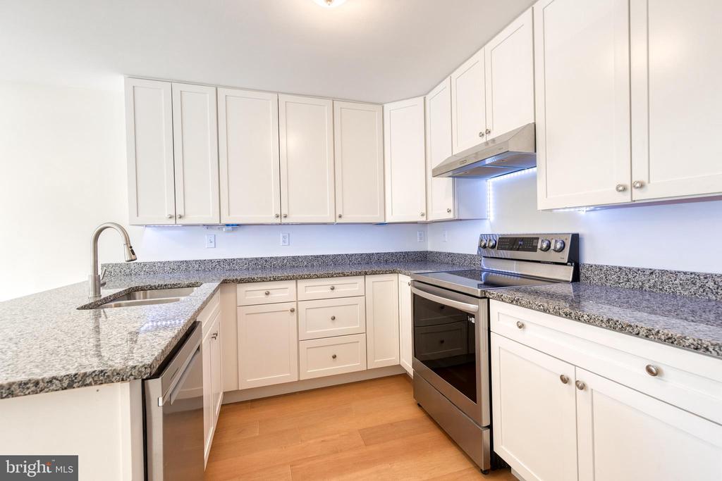 Kitchen with white cabinetry, granite counters, stainless steel appliances, and wood flooring.